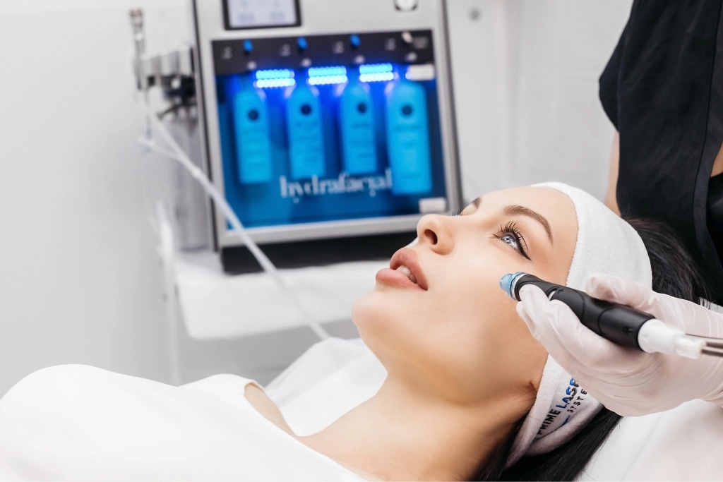Woman receiving HydraFacial treatment with professional machine and blue serums in background